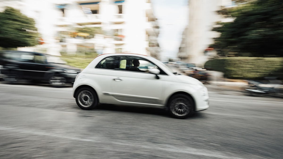 Dynamic capture of a compact white car speeding through a city street with motion blur effect.